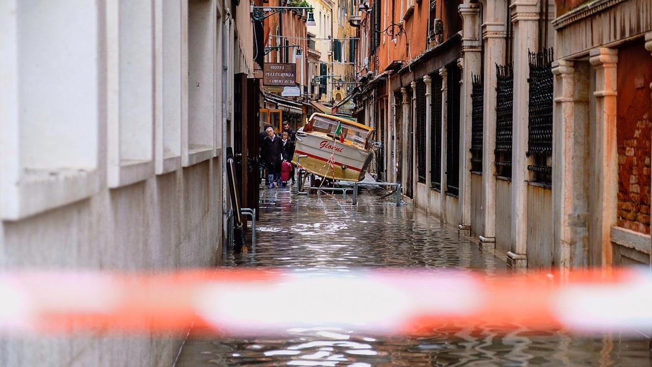 Eine überflutete enge Gasse in Venedig, in der ein kleines Boot gestrandet ist. Eine überflutete enge Gasse in Venedig, in der ein kleines Boot gestrandet ist.