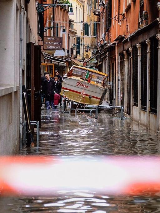 Eine überflutete enge Gasse in Venedig, in der ein kleines Boot gestrandet ist.