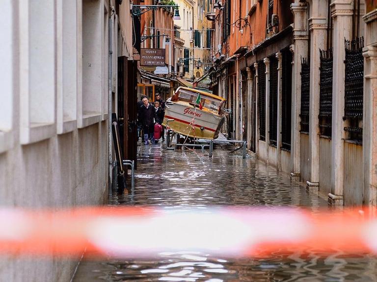 Eine überflutete enge Gasse in Venedig, in der ein kleines Boot gestrandet ist.