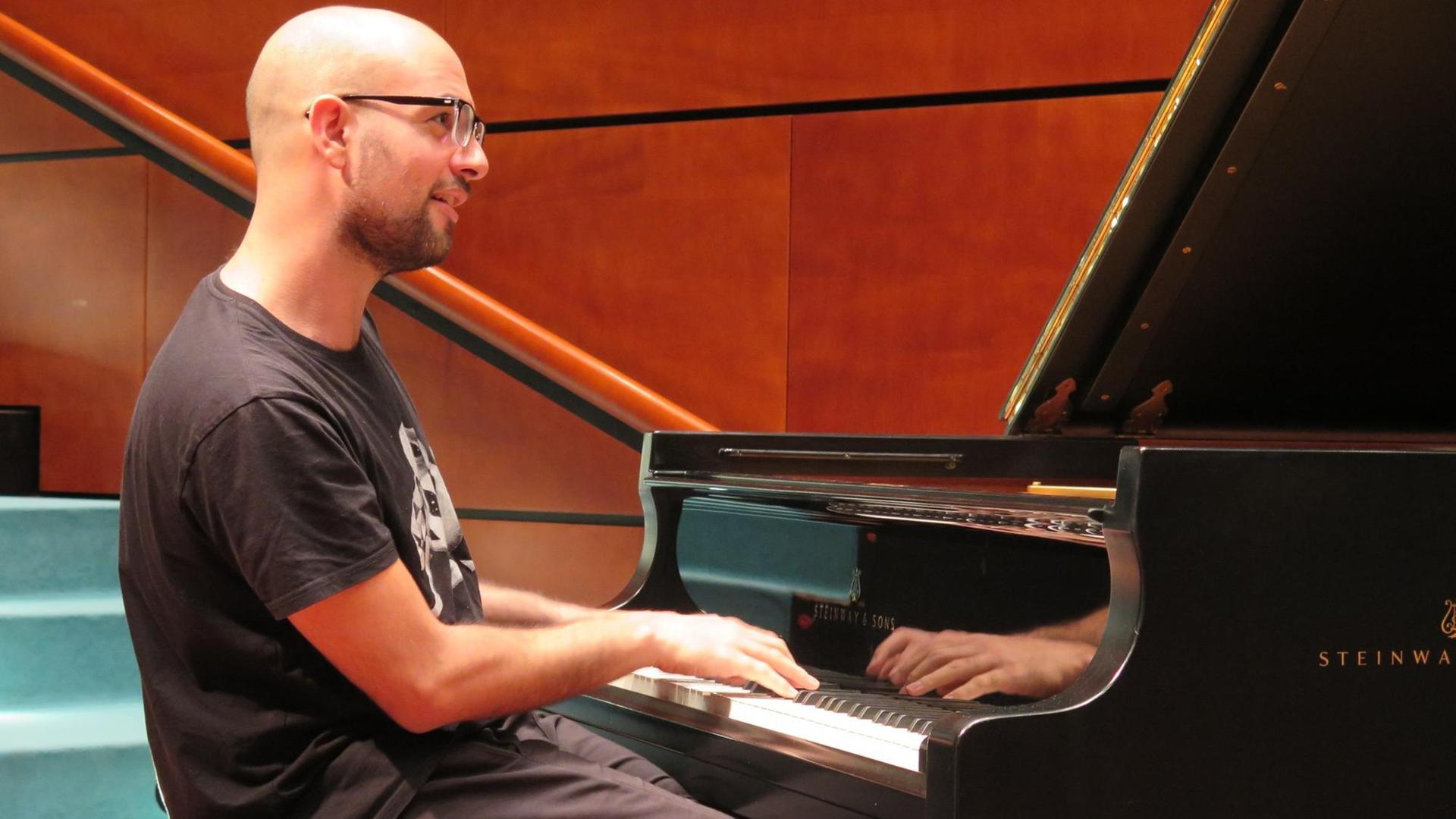 Ein junger Mann mit Glatze, T-Shirt und Brille sitzt am Konzertflügel und spielt.