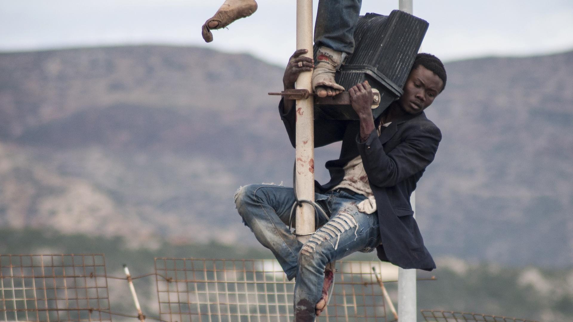Afrikanische Flüchtlinge klettern über den Grenzzaun in Melilla.