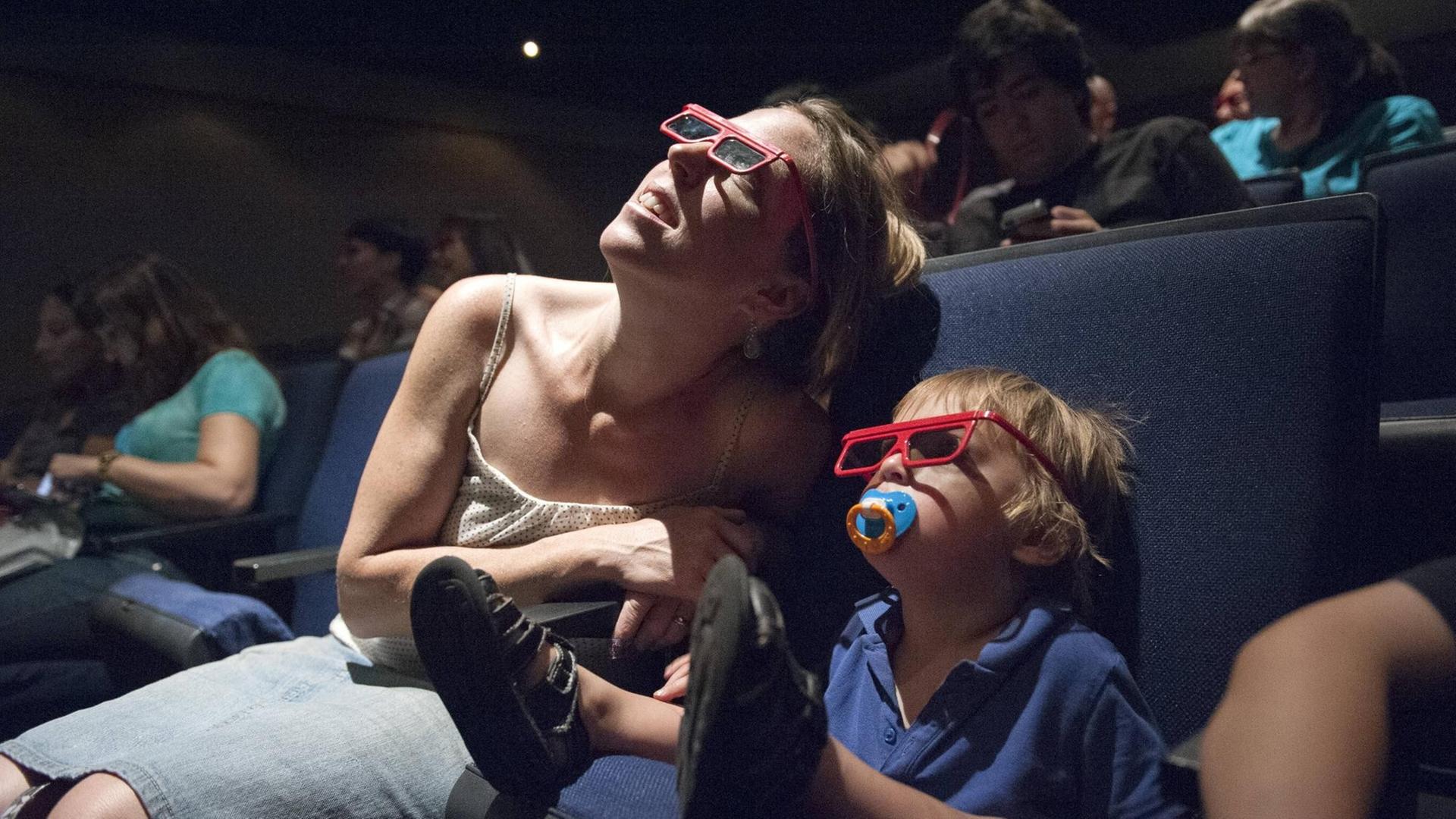 Eine Mutter mit Kleinkind schauen einen Film im 3D-Kino an.