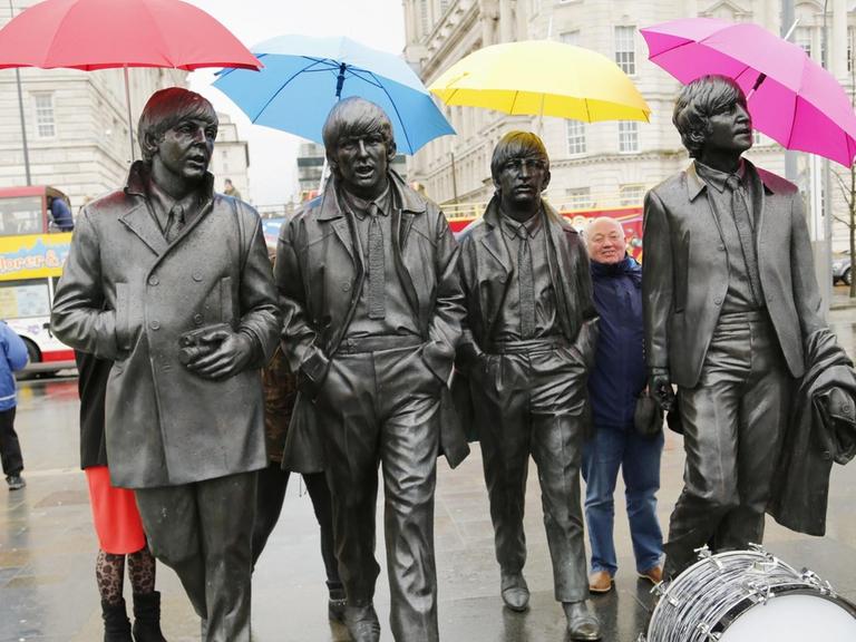 Liverpool feiert den 50. Geburtstag des Beatles Albums "Sgt. Pepper's Lonely Hearts Club Band". Menschen halten bunte Regenschirme über die Köpfe eines Denkmals zuehren der Gruppe.