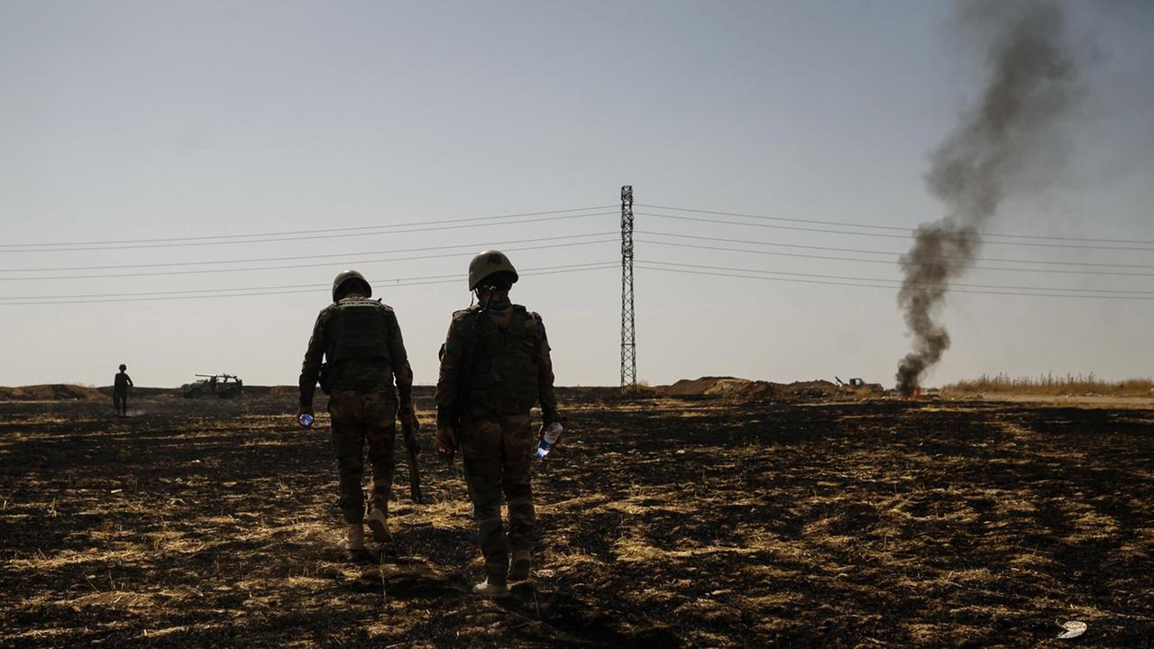 Eine karge Landschaft nahe Mossul. Zwei kurdische Soldaten laufen über ein Feld. Eine karge Landschaft nahe Mossul. Zwei kurdische Soldaten laufen über ein Feld.