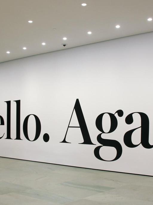 Menschen stehen am schwarzen Schriftzug "Hello Again" von Haim Steinbach im New Yorker Museum of Modern Art.