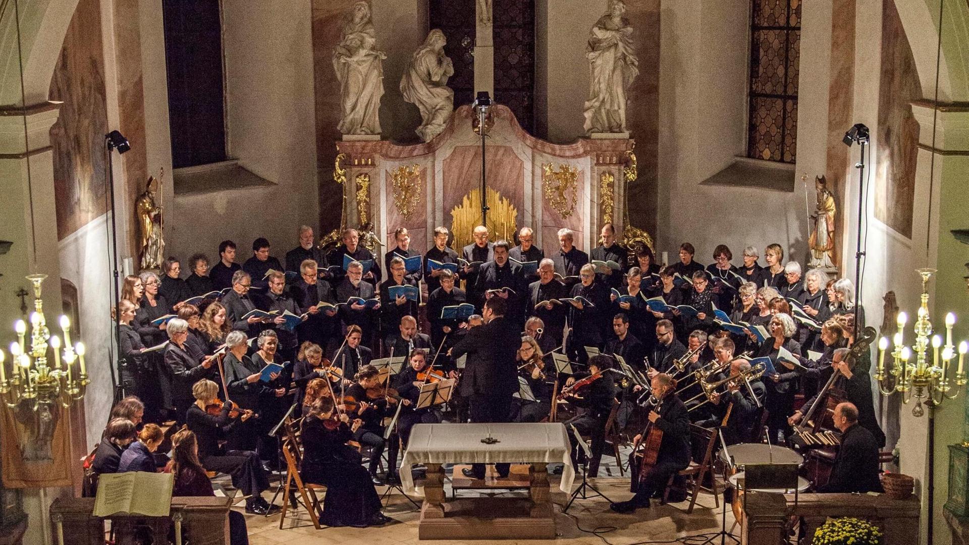 Das Bild zeigt den Chor mit Orchester bei einem Konzert vor dem Altar in der Kirche. Das Bild zeigt den Chor mit Orchester bei einem Konzert vor dem Altar in der Kirche.