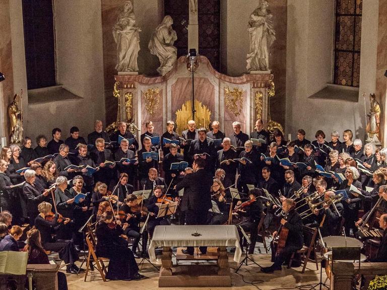 Das Bild zeigt den Chor mit Orchester bei einem Konzert vor dem Altar in der Kirche.