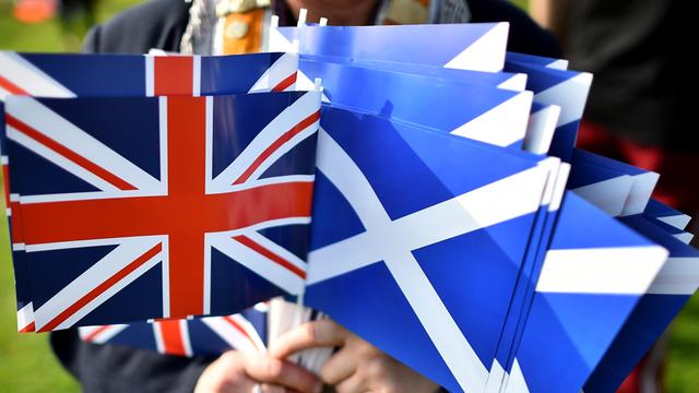 Ein Mann hält in der rechten Hand die Fahne von Großbritannien und in der linken die Fahne von Schottland