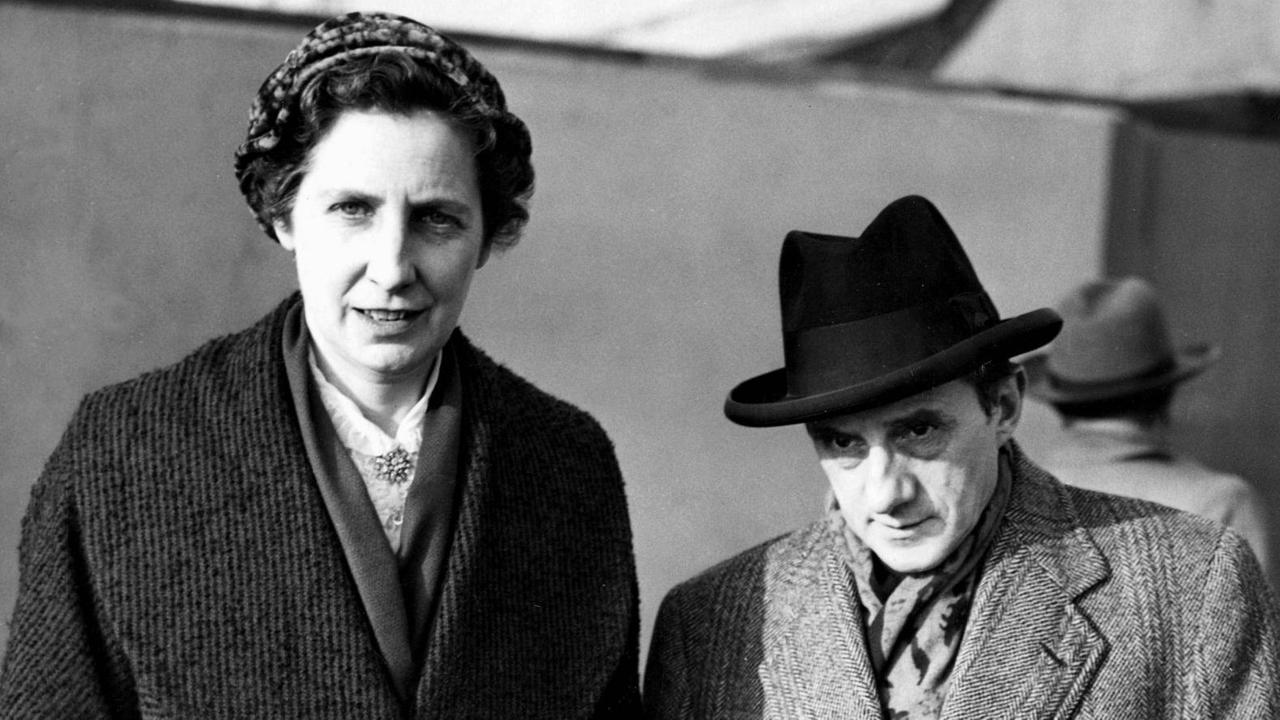 Eine große Frau steht neben einem deutlich kleineren Mann mit Hut. Eine große Frau steht neben einem deutlich kleineren Mann mit Hut.