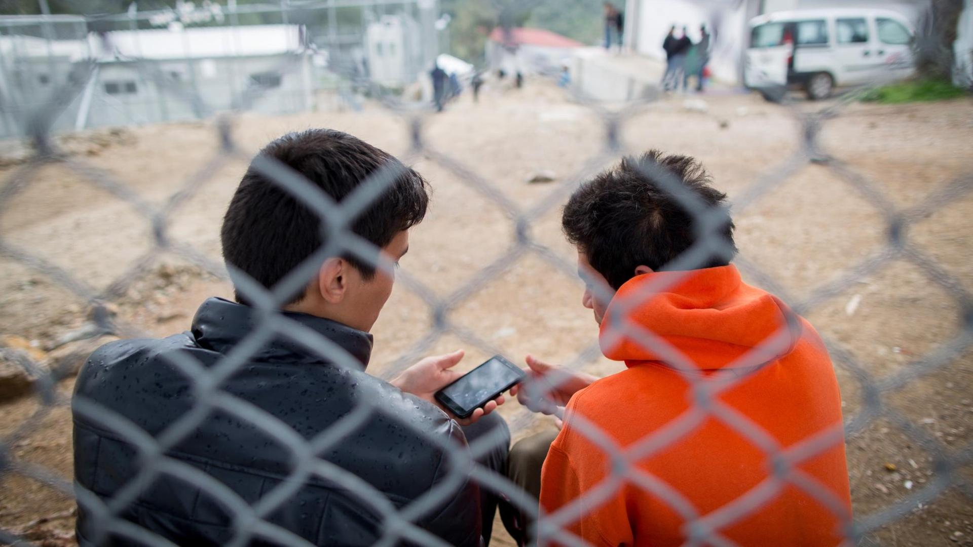 Flüchtlinge sitzen am 09.03.2016 in dem Flüchtlingscamp Moria auf der griechischen Insel Lesbos in der Hafenstadt Mitilini (Mytilini) hinter einem Zaun. Moria gilt als einer der größten Flüchtlings-Hotospots in Griechenland. Flüchtlinge sitzen am 09.03.2016 in dem Flüchtlingscamp Moria auf der griechischen Insel Lesbos in der Hafenstadt Mitilini (Mytilini) hinter einem Zaun. Moria gilt als einer der größten Flüchtlings-Hotospots in Griechenland.
