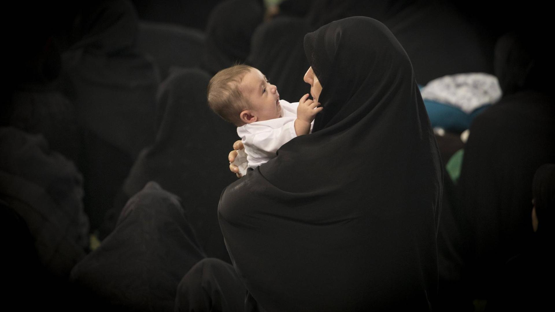 Eine iranische Mutter im schwarzen Tschador hält ihr Baby im Arm, Teheran. Eine iranische Mutter im schwarzen Tschador hält ihr Baby im Arm, Teheran.