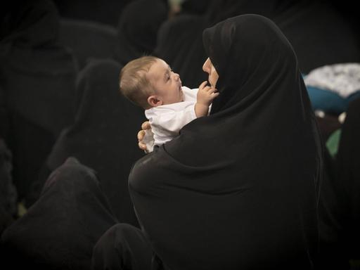 Eine iranische Mutter im schwarzen Tschador hält ihr Baby im Arm, Teheran.