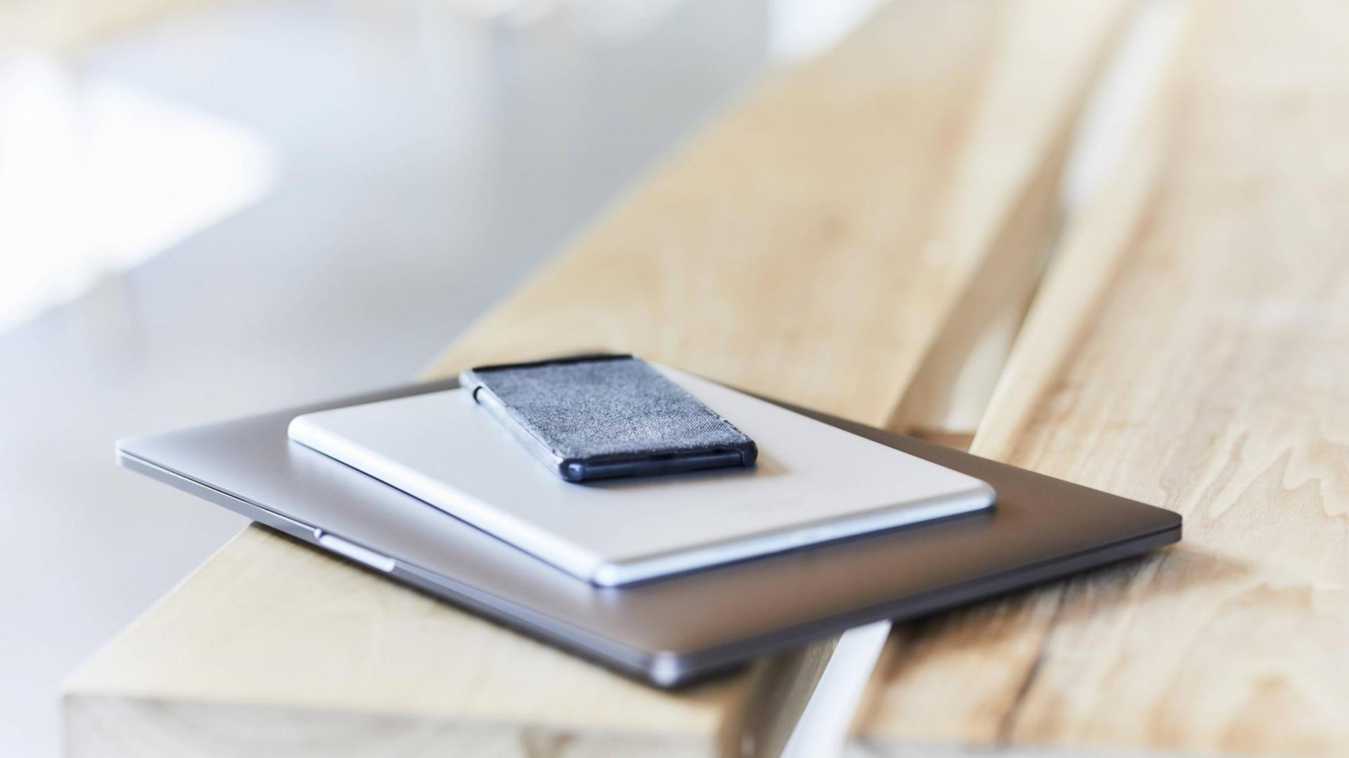 Laptop, Tablet und Smartphone liegen aufgestapelt auf einem Holztisch. Laptop, Tablet und Smartphone liegen aufgestapelt auf einem Holztisch.