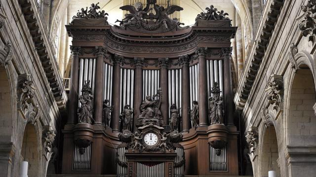 Orgelprospekt von dunklem Holz, vor den großen Pfeifen gibt es verschiedene Holzfiguren, die auch Instrumente bei sich haben, in der Mitte ist eine Uhr angebracht