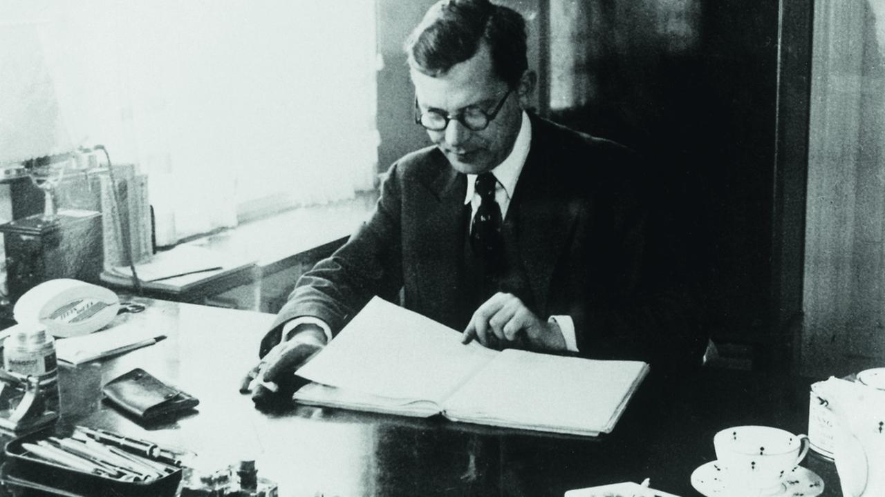 Hans Fallada sitzt mit einer Zigarette am Schreibtisch. Vor ihm ein aufgeschlagenes Buch. Hans Fallada sitzt mit einer Zigarette am Schreibtisch. Vor ihm ein aufgeschlagenes Buch.