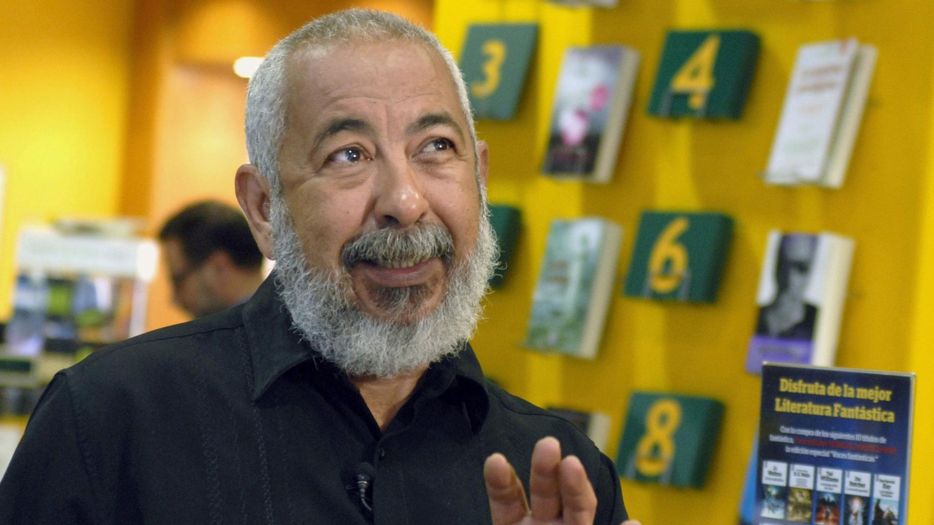 Der kubanische Schriftsteller Leonardo Padura gestikuliert und spricht. Hinter ihm sind Regale mit Büchern.