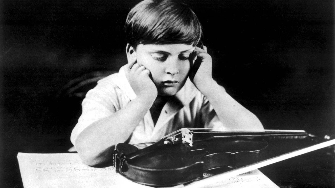 Yehudi Menuhin sitzt mit aufgestützem Kopf an einem Tisch, auf dem Notenblätter und seine Geige liegt. Yehudi Menuhin sitzt mit aufgestützem Kopf an einem Tisch, auf dem Notenblätter und seine Geige liegt.