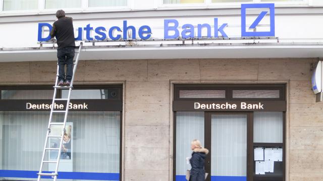 An einer Filiale der Deutschen Bank in München repariert ein Arbeiter den Schriftzug. 