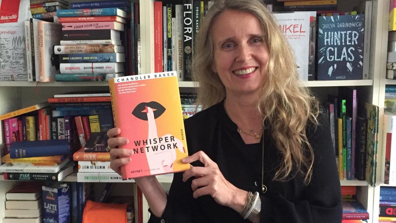 Lesart-Redakteurin Kim Kindermann steht mit dem Buch "Whisper Network" von Chandler Baker vor einem Bücherregal. Lesart-Redakteurin Kim Kindermann steht mit dem Buch "Whisper Network" von Chandler Baker vor einem Bücherregal.