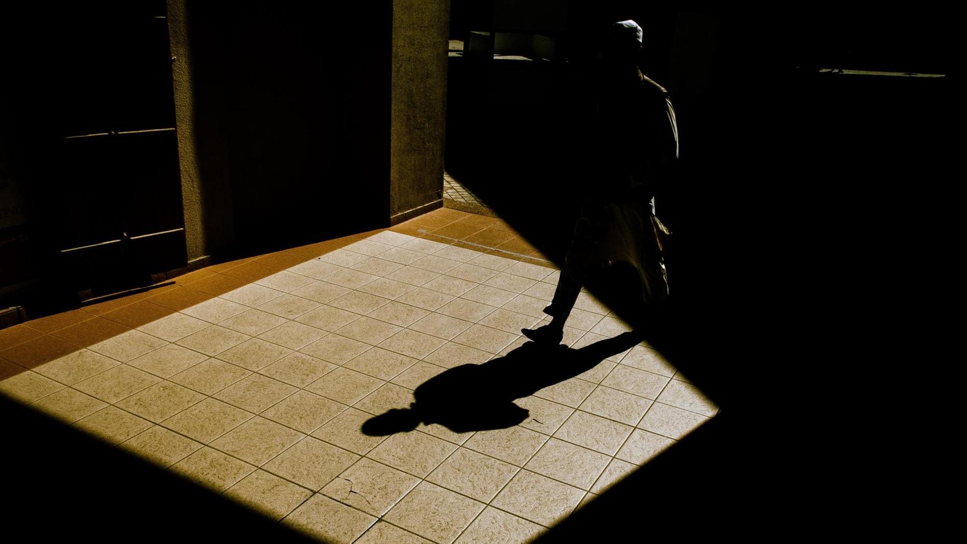 Mann läuft durch nächtliche Straßen, vor ihm sein Schatten.
