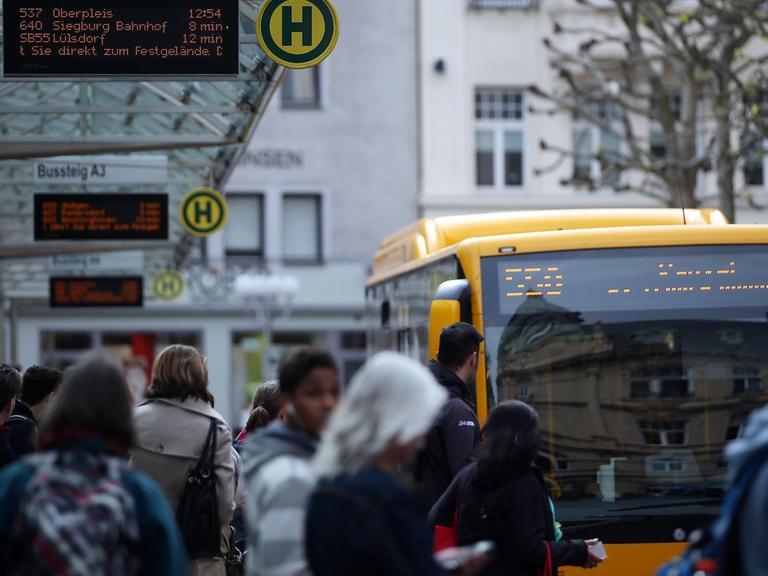 Menschen warten an einer Bushaltestelle in Bonn.
