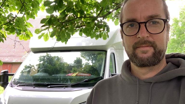 Jens Nähler macht ein Selbstporträt mit seinem Wohnmobil im Hintergrund. Jens Nähler macht ein Selbstporträt mit seinem Wohnmobil im Hintergrund.