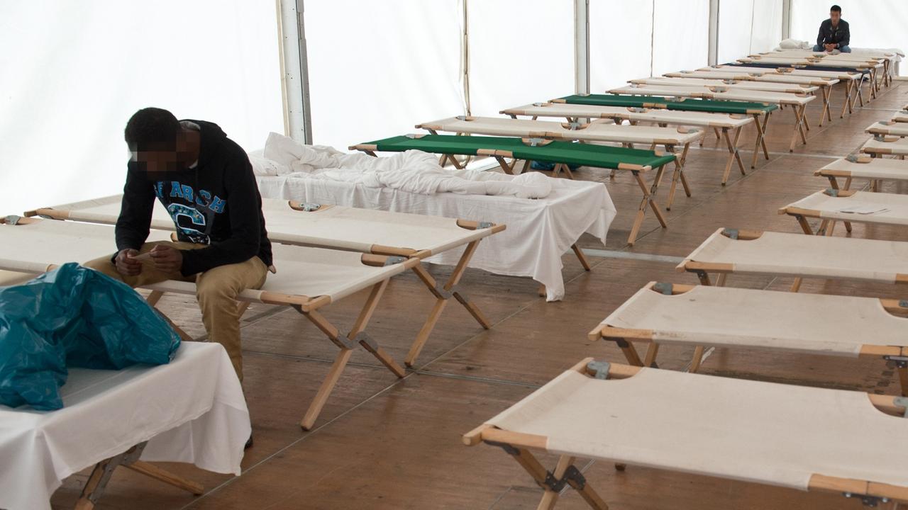 Flüchtlinge sitzen auf Feldbetten in einem Zelt der Hessischen Erstaufnahmeeinrichtung in Gießen.