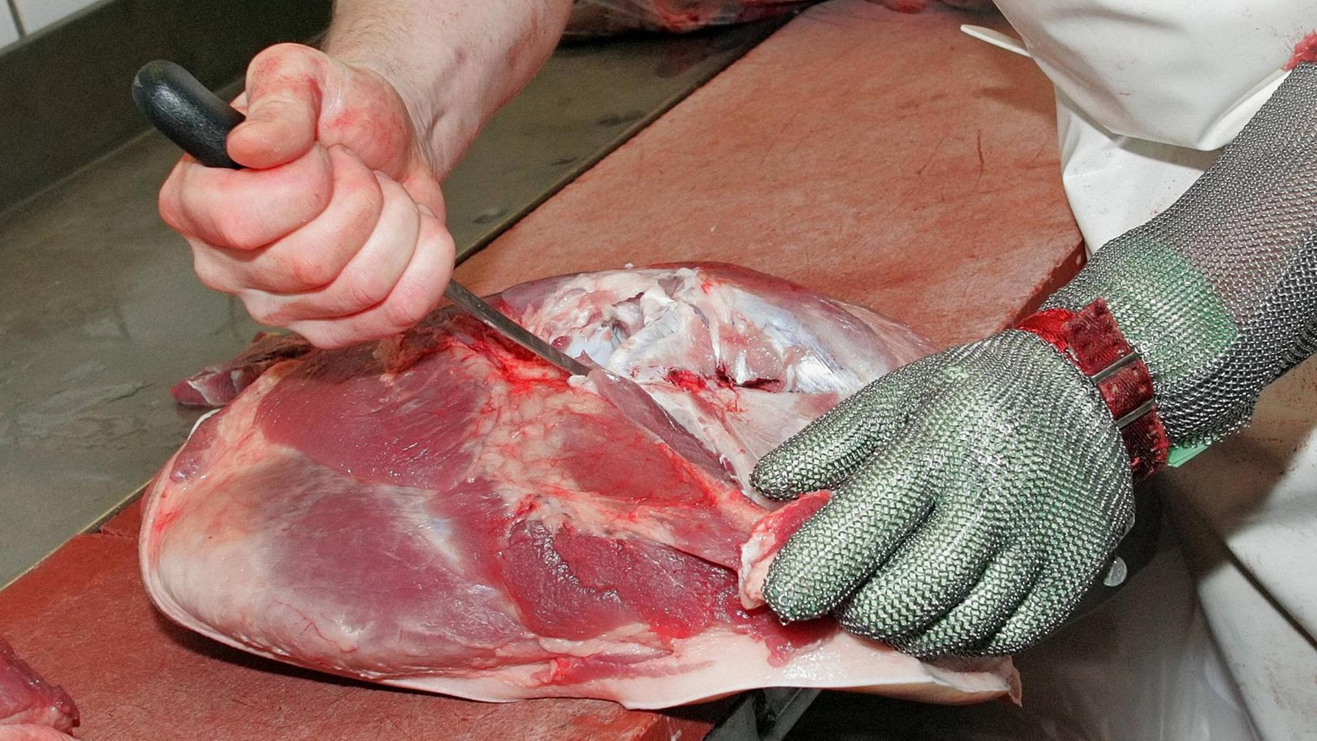 Mit einem Messer schneidet ein Schlachter einen Knochen aus einem Stück Schweinefleisch. Mit einem Messer schneidet ein Schlachter einen Knochen aus einem Stück Schweinefleisch.