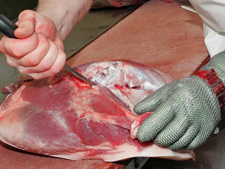 Mit einem Messer schneidet ein Schlachter einen Knochen aus einem Stück Schweinefleisch.