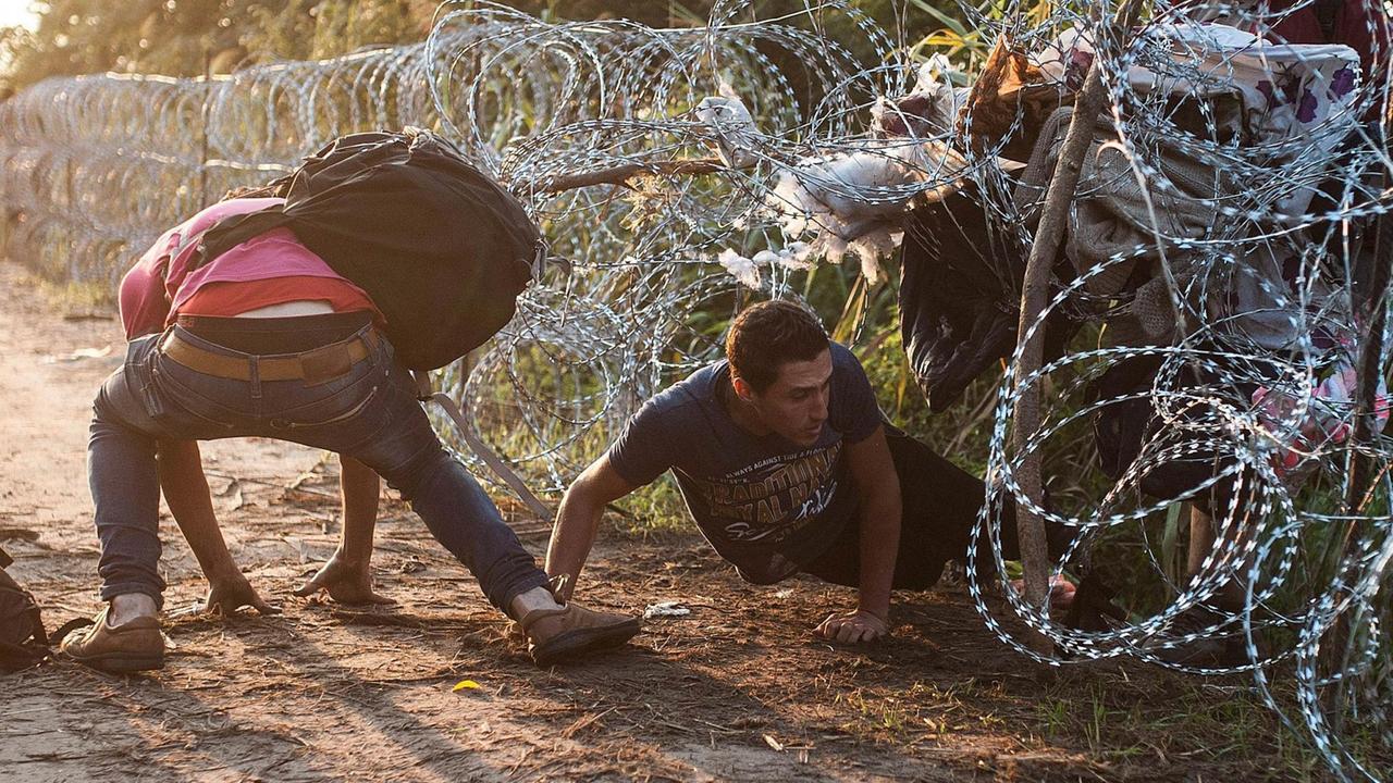 Zwei Männer steigen unter einem Stacheldrahtzaun hindurch Zwei Männer steigen unter einem Stacheldrahtzaun hindurch
