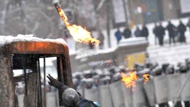 Demonstranten in der Hauptstadt werfen eine Brandbombe auf Polizisten, die Schutzschilder vor sich halten.