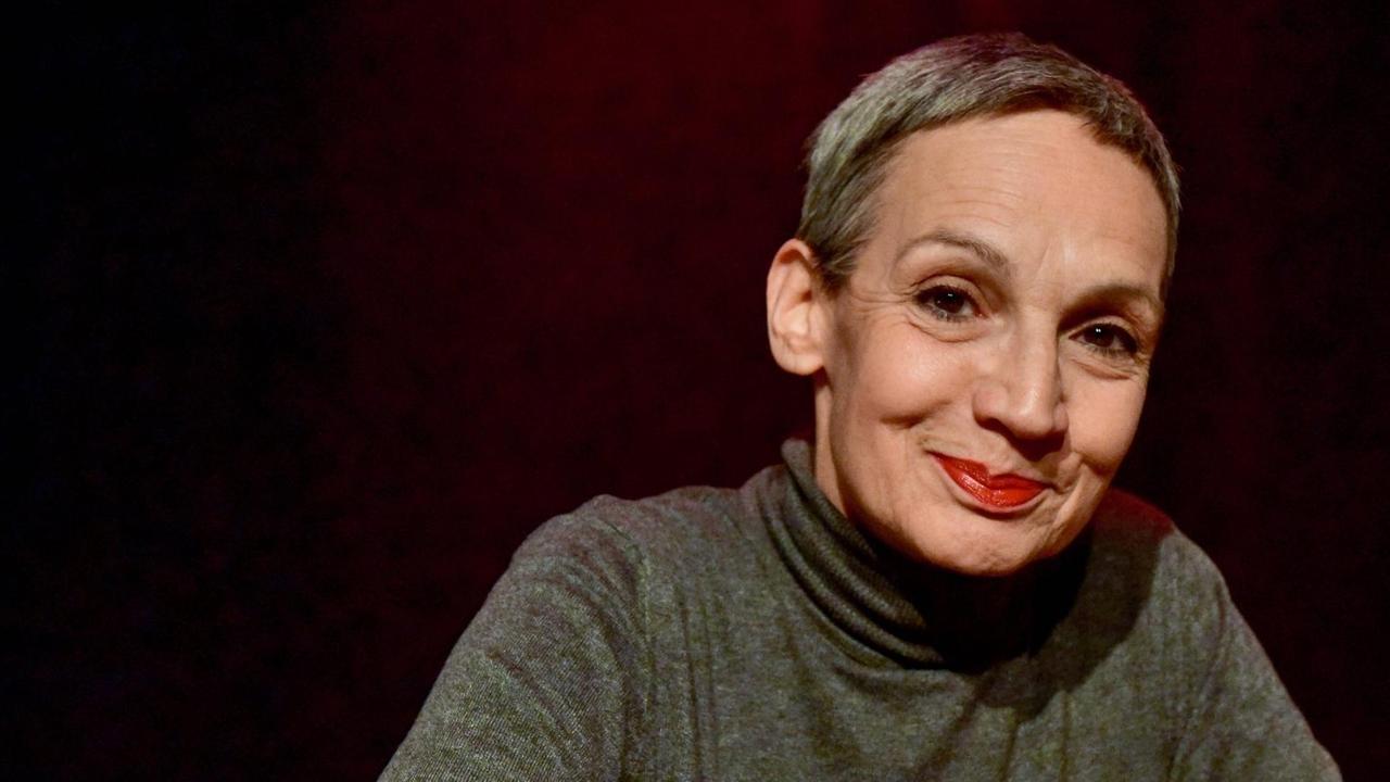 Porträt von Marion Brasch mit kurzen, grauen Haaren und rotem Lippenstift vor einem dunklen Theatervorhang. Porträt von Marion Brasch mit kurzen, grauen Haaren und rotem Lippenstift vor einem dunklen Theatervorhang.