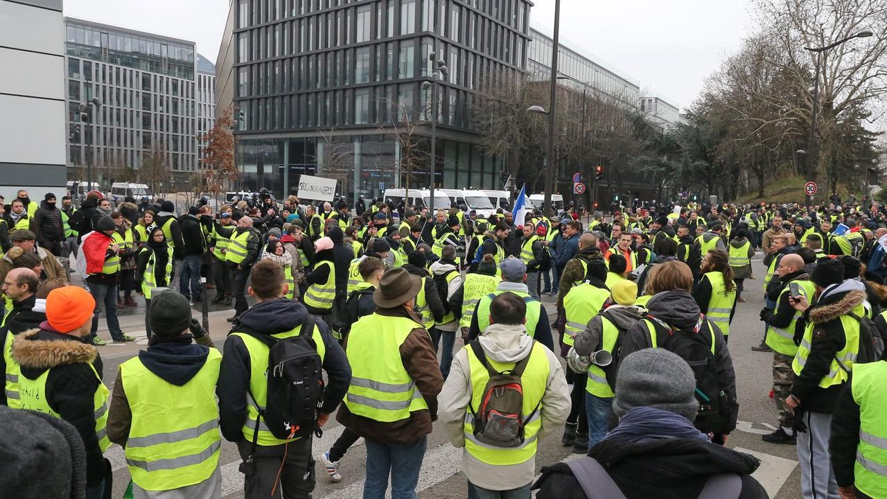 In Paris protestieren Anhänger der sogenannten "Gelbwesten", im Hintergrund ist ein Bürogebäude zu sehen. In Paris protestieren Anhänger der sogenannten "Gelbwesten", im Hintergrund ist ein Bürogebäude zu sehen.