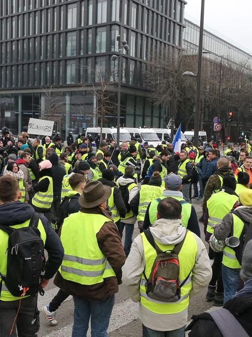 In Paris protestieren Anhänger der sogenannten "Gelbwesten", im Hintergrund ist ein Bürogebäude zu sehen.  