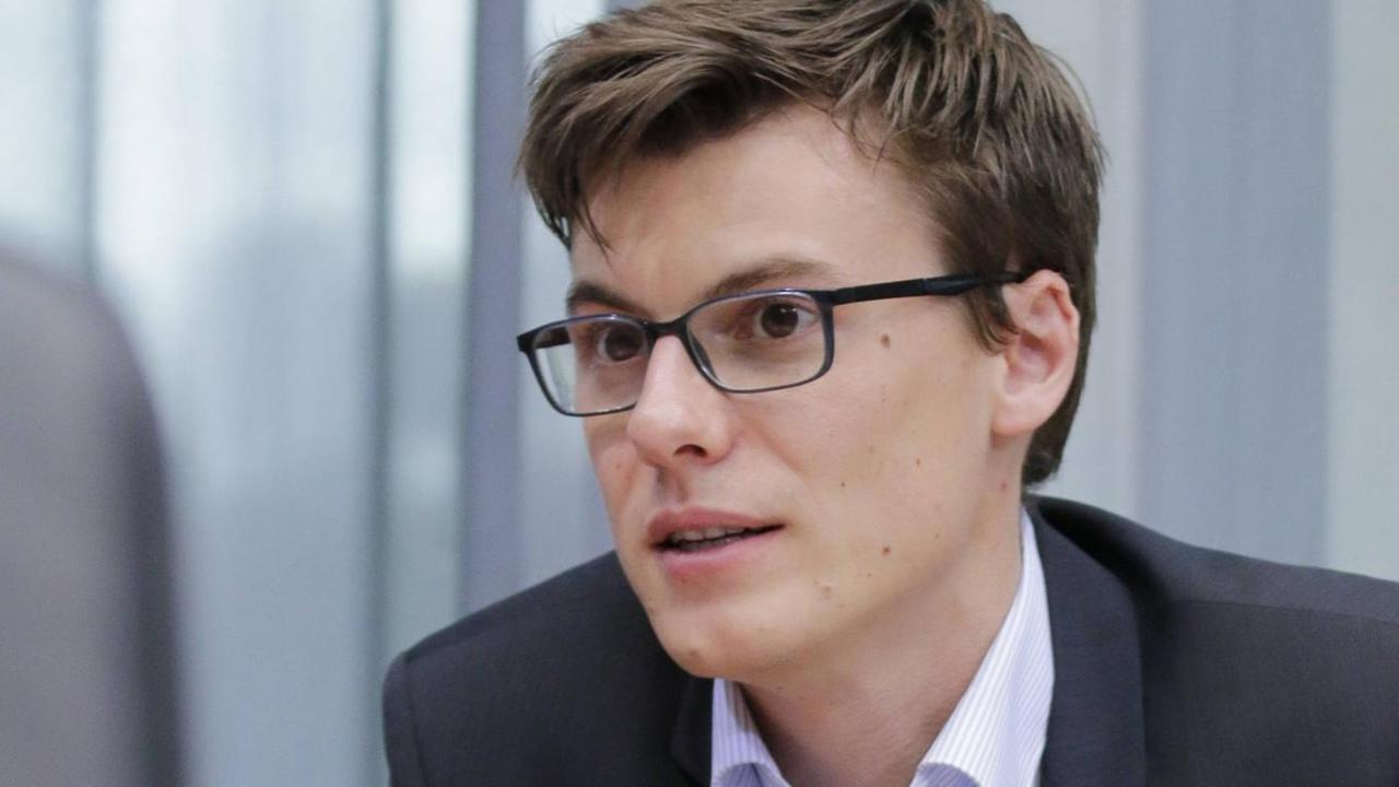Ein junger Mann im Anzug, mit Brille und kurzen brauen Haaren, spricht mit der Hand gestikulierend Ein junger Mann im Anzug, mit Brille und kurzen brauen Haaren, spricht mit der Hand gestikulierend