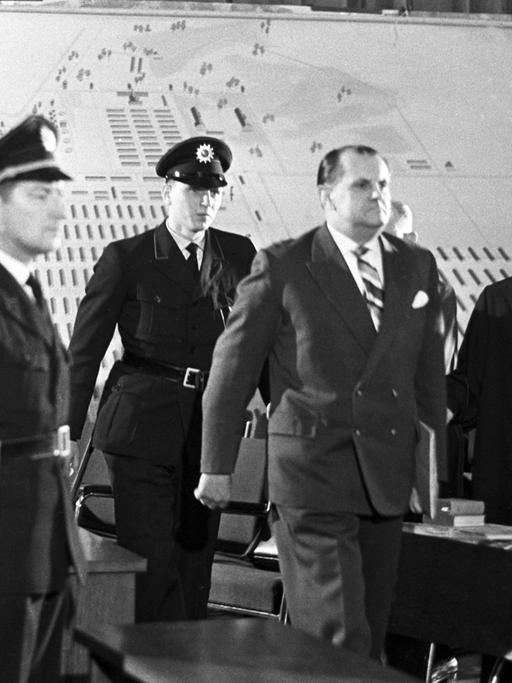 Der Angeklagte Oswald Kaduk wird von drei Polizisten in einen Gerichtssaal geführt.