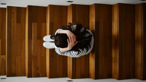 Illustrationsfoto zum Thema Depressionen: Eine Frau kauert auf einer Treppe. Das Foto zeigt sie von oben. Sie hat die Arme um ihren Körper geschlungen. Foto: Frank May/picture alliance (model released) | Verwendung weltweit