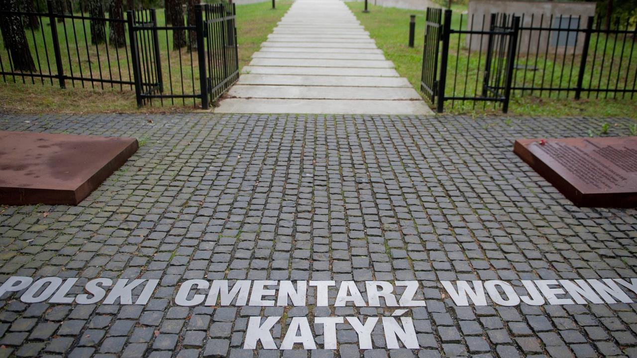 Blick auf einen Friedhof durch das Eingangstor, auf dem Boden stehen die Worte: Polski Cmentarz Wojenny Katyn Blick auf einen Friedhof durch das Eingangstor, auf dem Boden stehen die Worte: Polski Cmentarz Wojenny Katyn