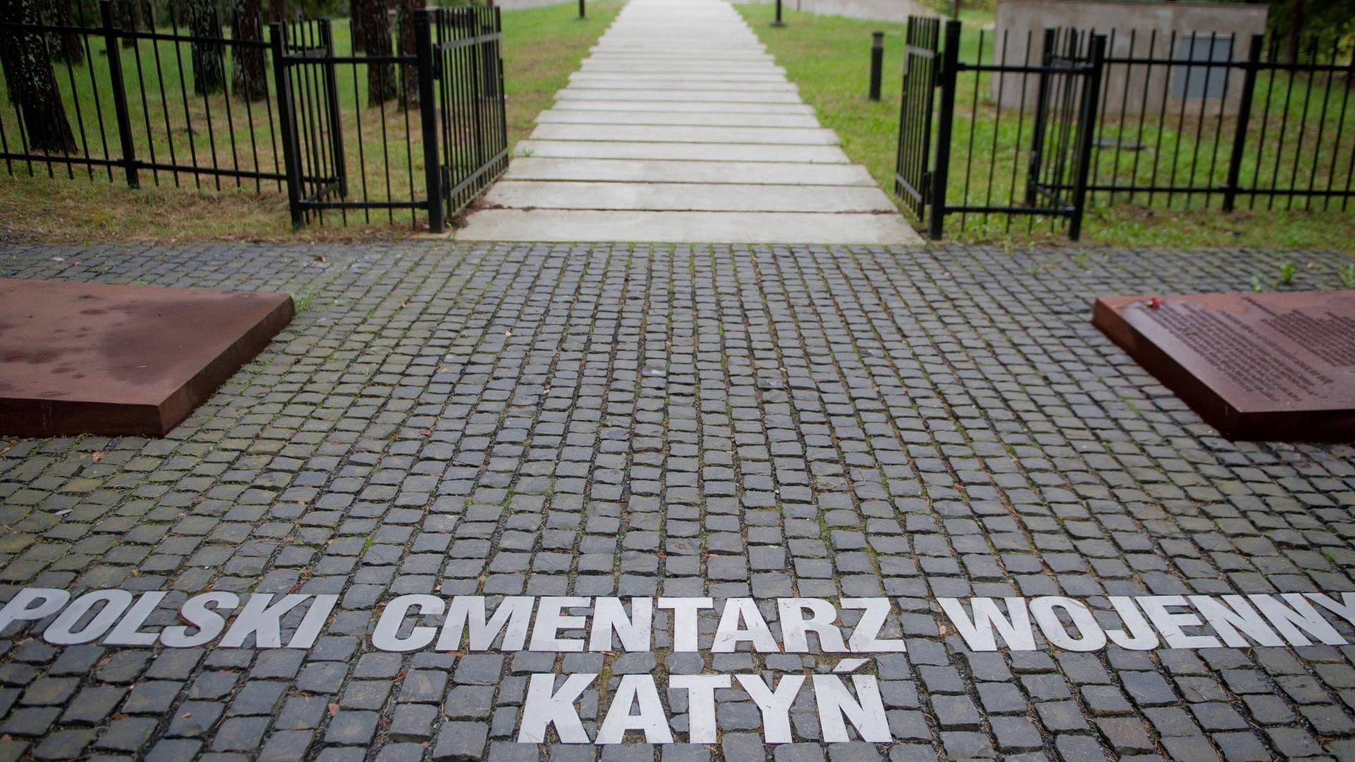 Blick auf einen Friedhof durch das Eingangstor, auf dem Boden stehen die Worte: Polski Cmentarz Wojenny Katyn Blick auf einen Friedhof durch das Eingangstor, auf dem Boden stehen die Worte: Polski Cmentarz Wojenny Katyn