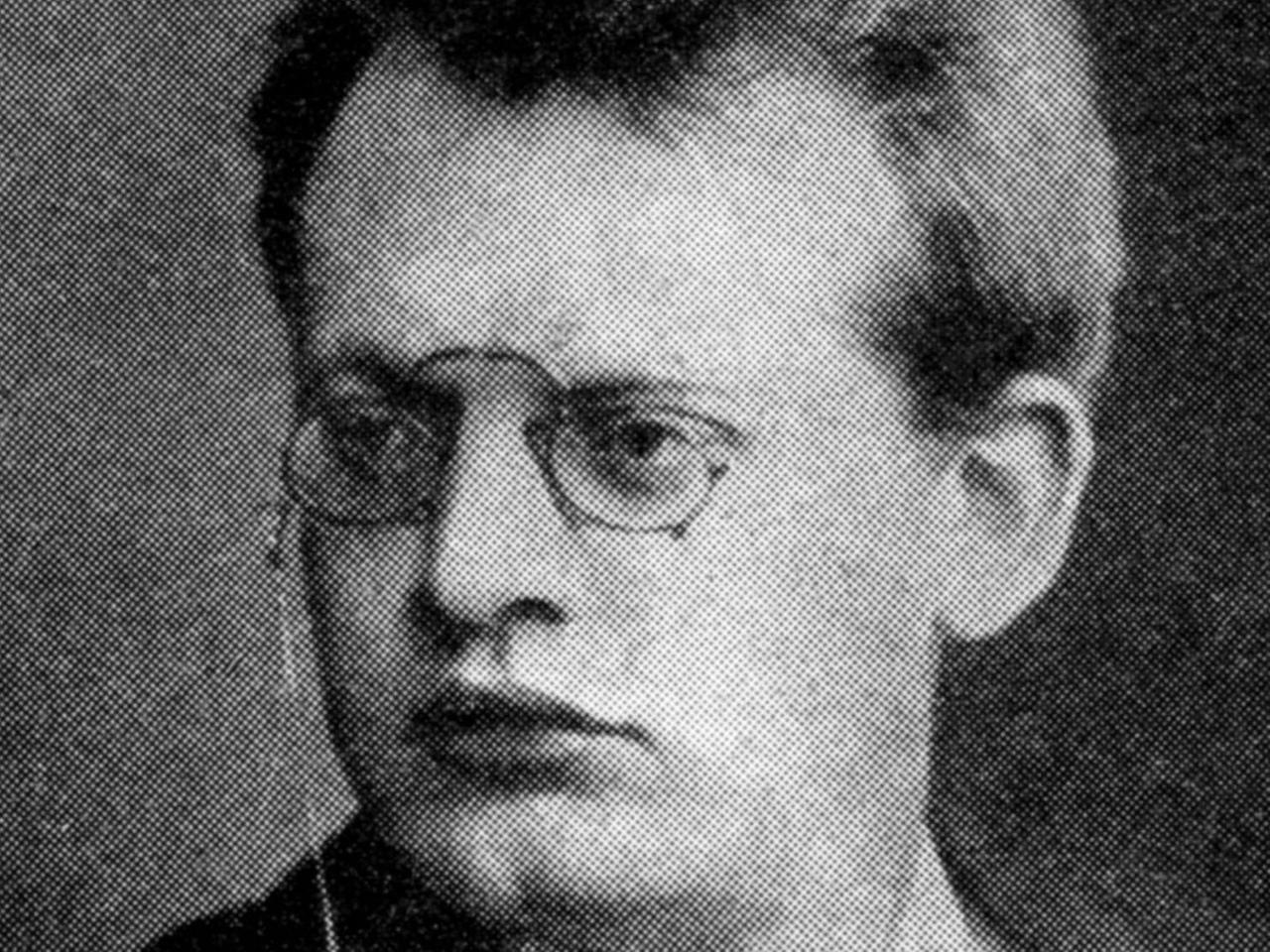Schwarz-weiß-Aufnahme eines Mannes mit Brille, üppigen Lippen und einem ernsten Gesichtsausdruck.