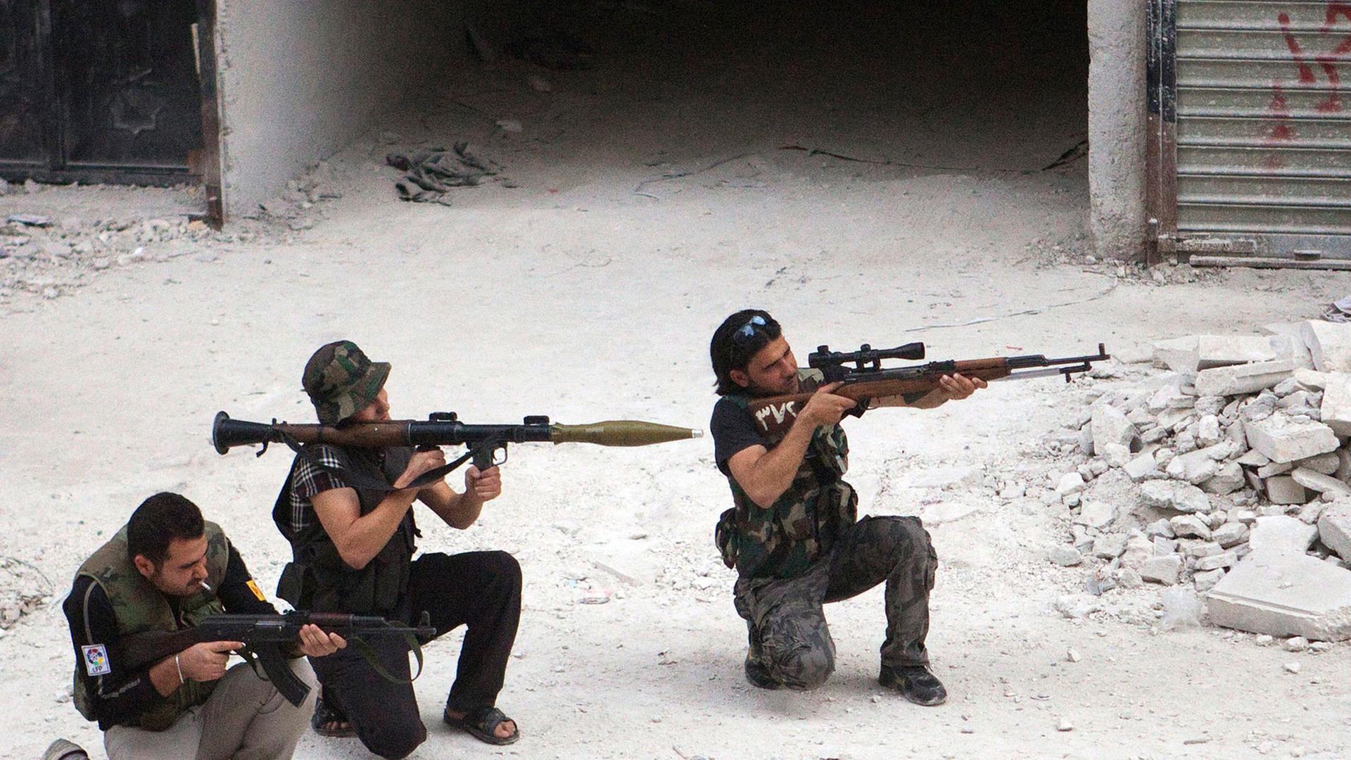 Drei Kämpfer der Freien Syrischen Armee knien mit ihren Gewehren in den Händen auf dem Boden einer Straße in der syrischen Stadt Aleppo.