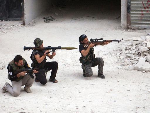 Drei Kämpfer der Freien Syrischen Armee knien mit ihren Gewehren in den Händen auf dem Boden einer Straße in der syrischen Stadt Aleppo.