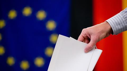 Ein Wähler gibt am 25.05.2014 in Berlin-Mitte seinen Stimmzettel für die Europawahl und den Volksentscheid für das Tempelhofer Feld ab. Im Hintergrund sind eine Europa- und eine Deutschlandfahne zu sehen.