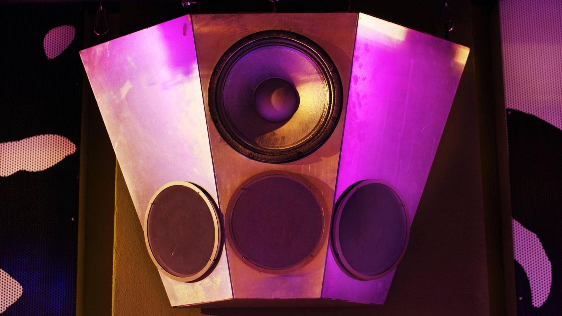 Eine Lautsprecherbox hängt in einer Disco und wird durch das Licht leicht lilafarben angestrahlt