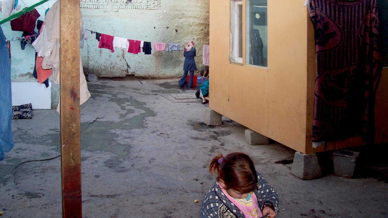 Blick in den Innenhof einer Haftanstalt für Frauen in Mazar-e-Sharif in Nordafghanistan, im Vordergrund ist ein Kind zu sehen, hinten eine Wäscheleine und zwei Frauen beim Wäschewaschen