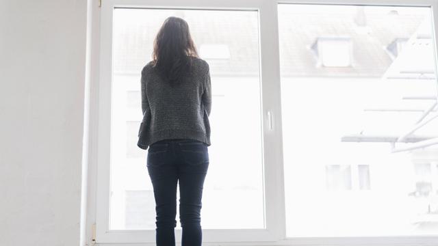 Ein Frau steht an einem Fenster und blickt in die Ferne.