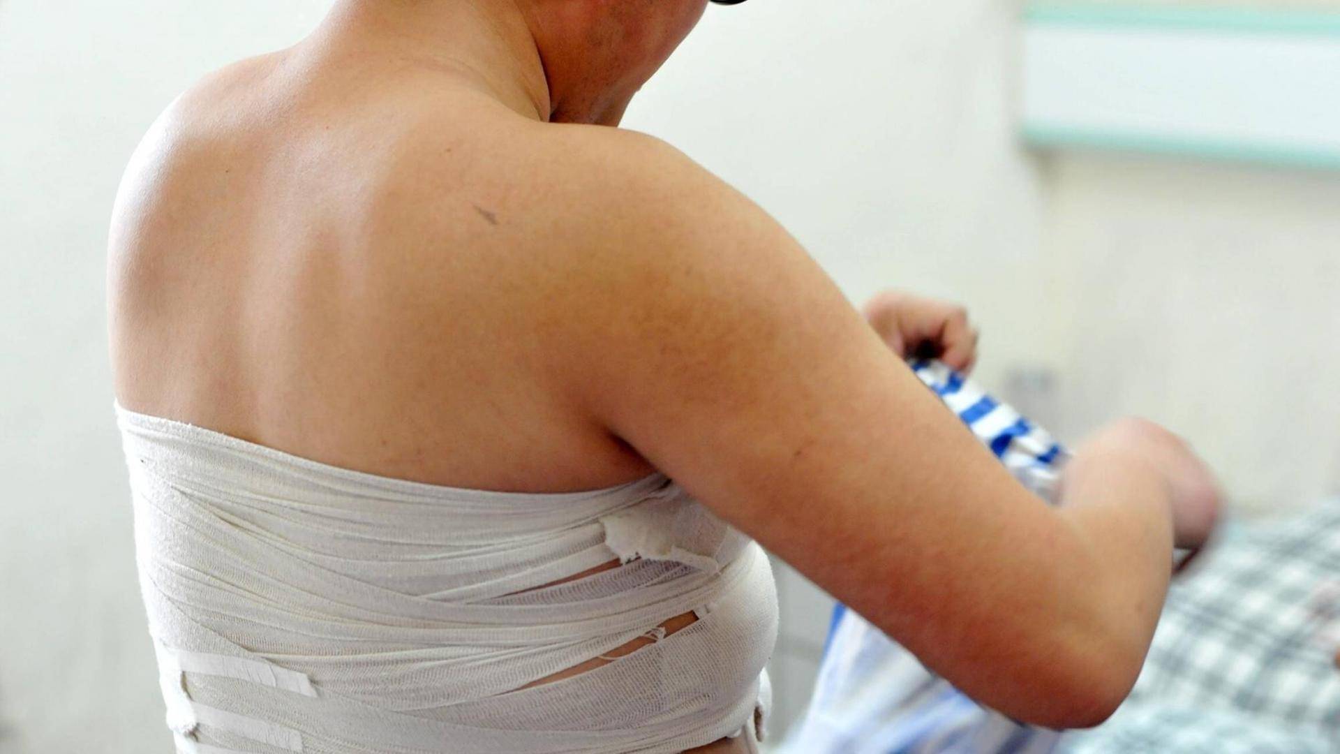 Eine Frau mit kurzen Haaren, Rückensicht, mit Bandagen um die Brüste herumgewickelt Eine Frau mit kurzen Haaren, Rückensicht, mit Bandagen um die Brüste herumgewickelt