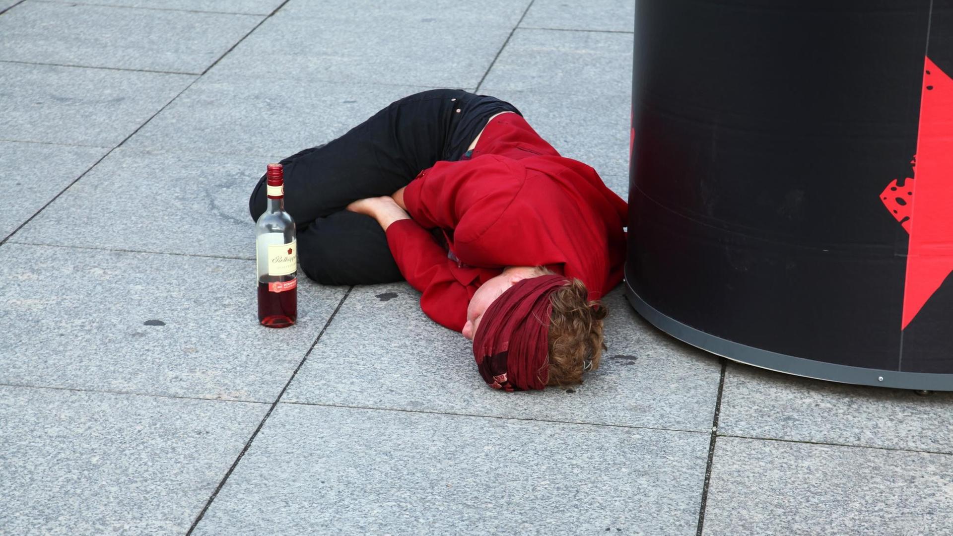 Eine junge Frau liegt völlig betrunken auf dem Pflaster an einer Plakatsäule Eine junge Frau liegt völlig betrunken auf dem Pflaster an einer Plakatsäule