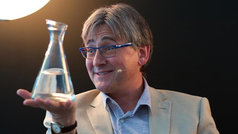 Callum Roberts hält eine Glasflasche mit Wasser auf der ausgestreckten Hand Callum Roberts hält eine Glasflasche mit Wasser auf der ausgestreckten Hand