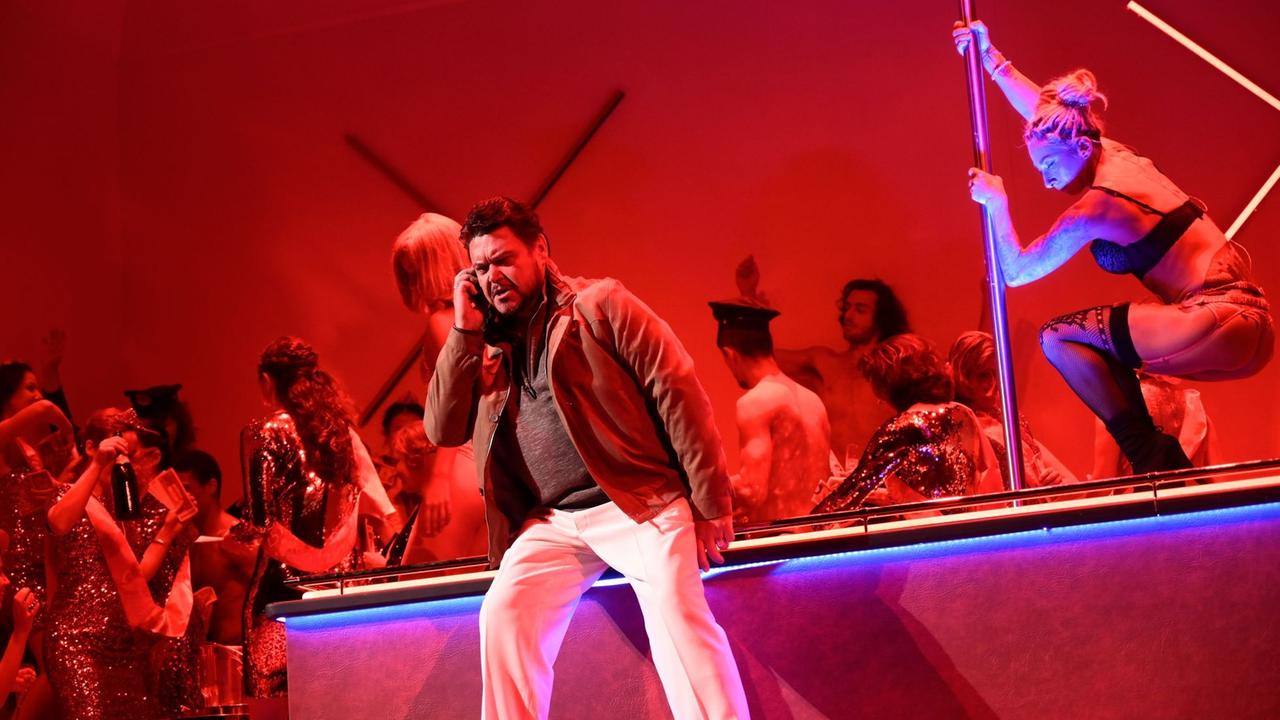 Ein Mann telefoniert zornig in einem rot ausgeleuchteten Nachtclub. Im Hintergrund tanzt eine Stripperin an der Stange. Ein Mann telefoniert zornig in einem rot ausgeleuchteten Nachtclub. Im Hintergrund tanzt eine Stripperin an der Stange.
